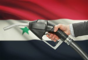 Fuel pump nozzle in hand with flag on background - Syria