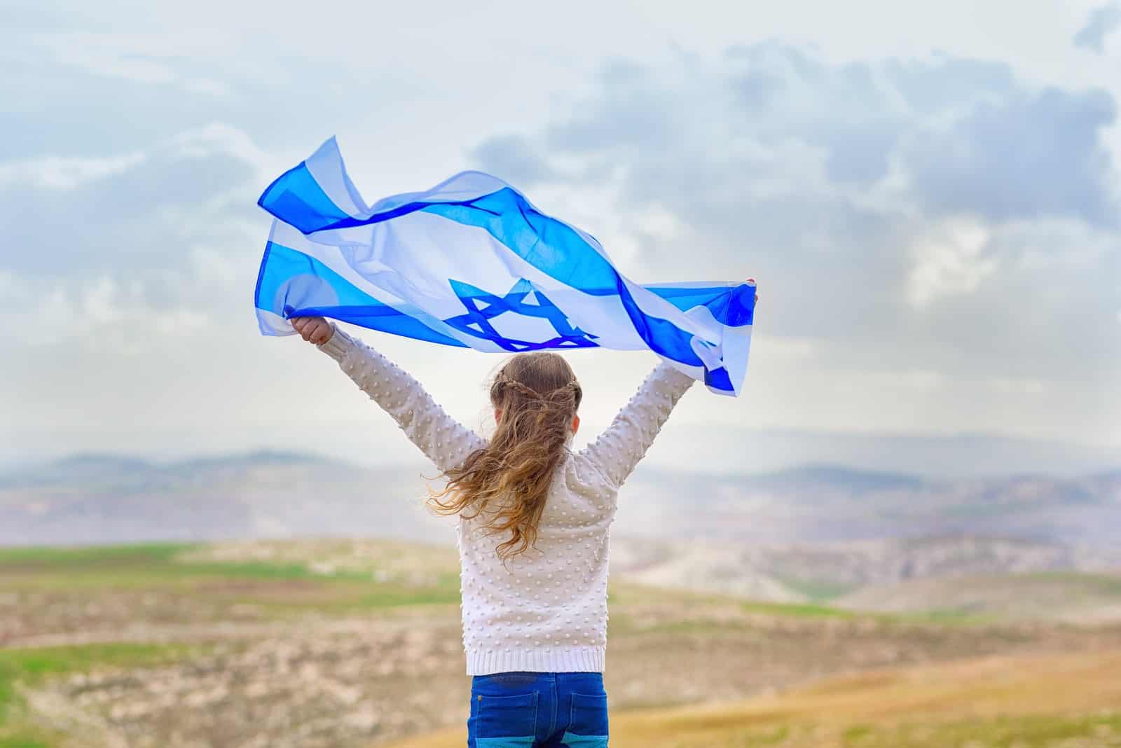 Little patriot jewish girl standing and enjoying with the flag of Israel on blue sky background.Memorial day-Yom Hazikaron, Patriotic holiday Independence day Israel - Yom Haatzmaut concept