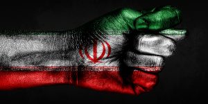 A hand with a painted Iran flag shows a fig, a sign of aggression, disagreement, a dispute on a dark background. Horizontal frame