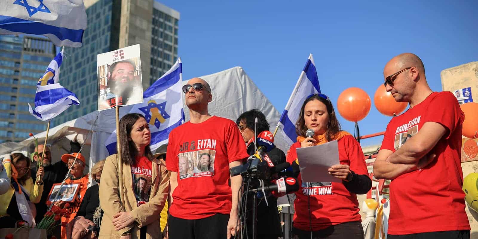 Farewell to Bibas Family A woman in an orange shirt speaks into a microphone while standing beside others at a public gathering in Tel Aviv, Israel, on February 26, 2025. A funeral is being held for the former hostages, whose bodies were returned to Israel from Gaza last week after being abducted from Kibbutz Nir Oz on October 7, 2023.